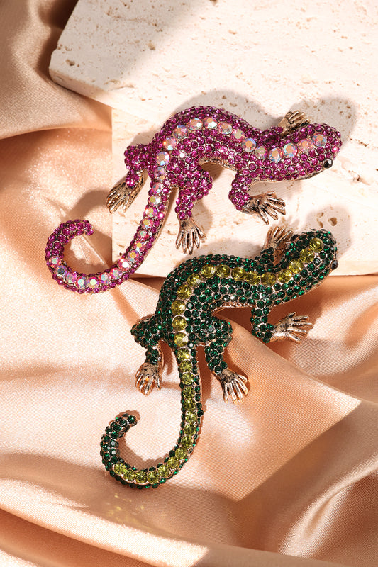 Two gecko brooches, green with yellow crystals and fuchsia with iridescent crystals, on silky fabric and stone