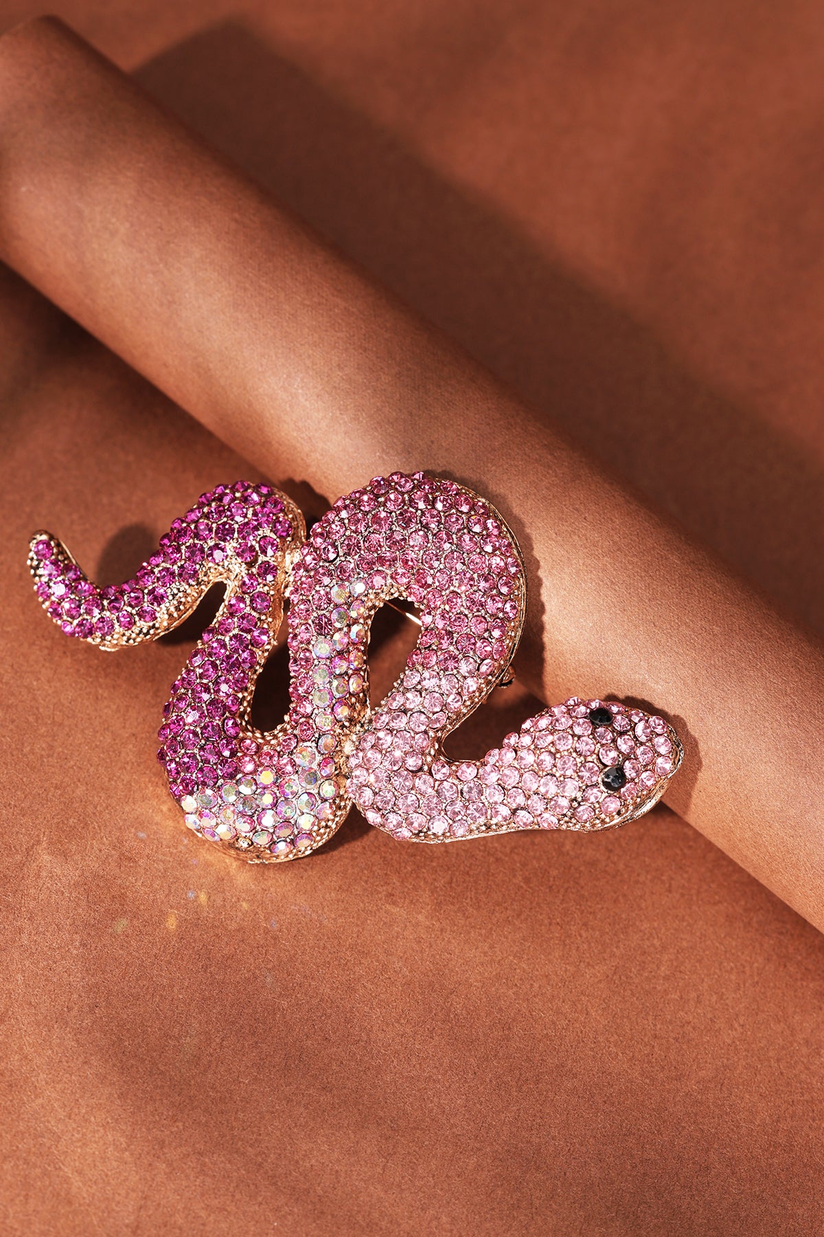 Close-up of pink and purple crystal snake brooch on brown paper rolled background