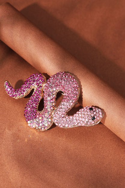 Close-up of pink and purple crystal snake brooch on brown paper rolled background