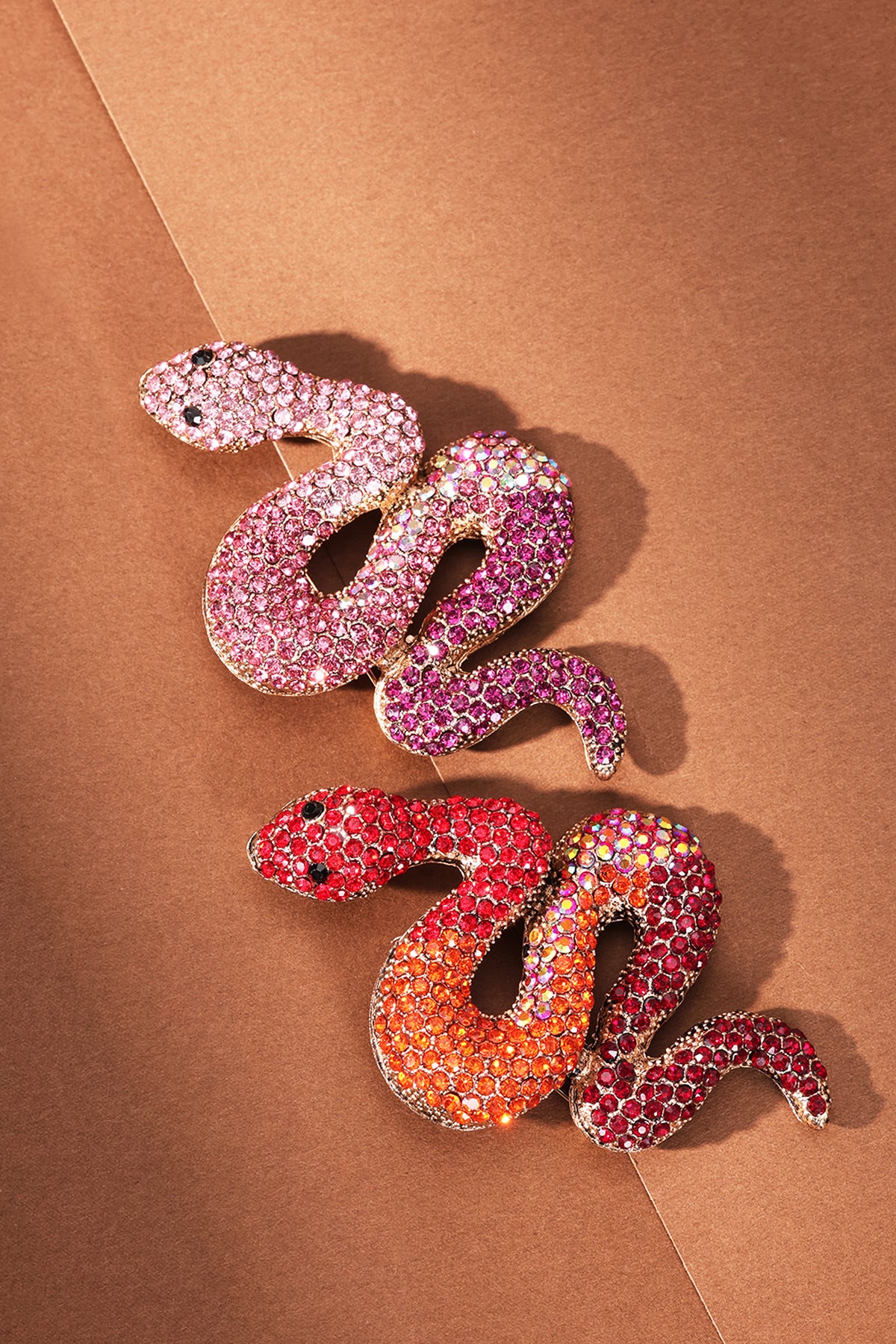 Two crystal snake brooches in pink and red shades placed on brown paper background