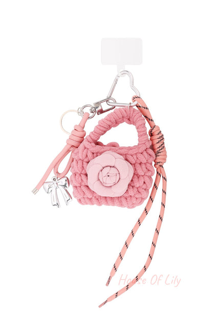 Pink knitted bag-shaped keychain with flower applique, silver bow charm, and pink cord on white background
