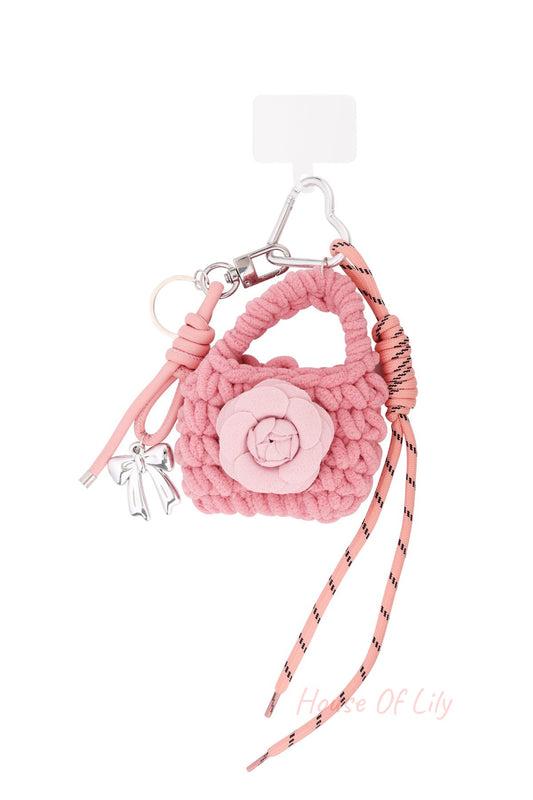 Pink knitted bag-shaped keychain with flower applique, silver bow charm, and pink cord on white background
