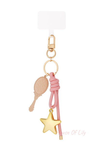 Close-up of chic bag charm with golden star pendant, pink knotted leather and vintage-style mirror pendant on white background