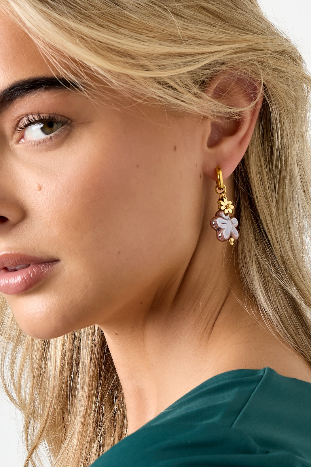 Close-up profile of woman with blonde hair wearing gold hoop earring with mauve-lilac flower charm and gold flower accent