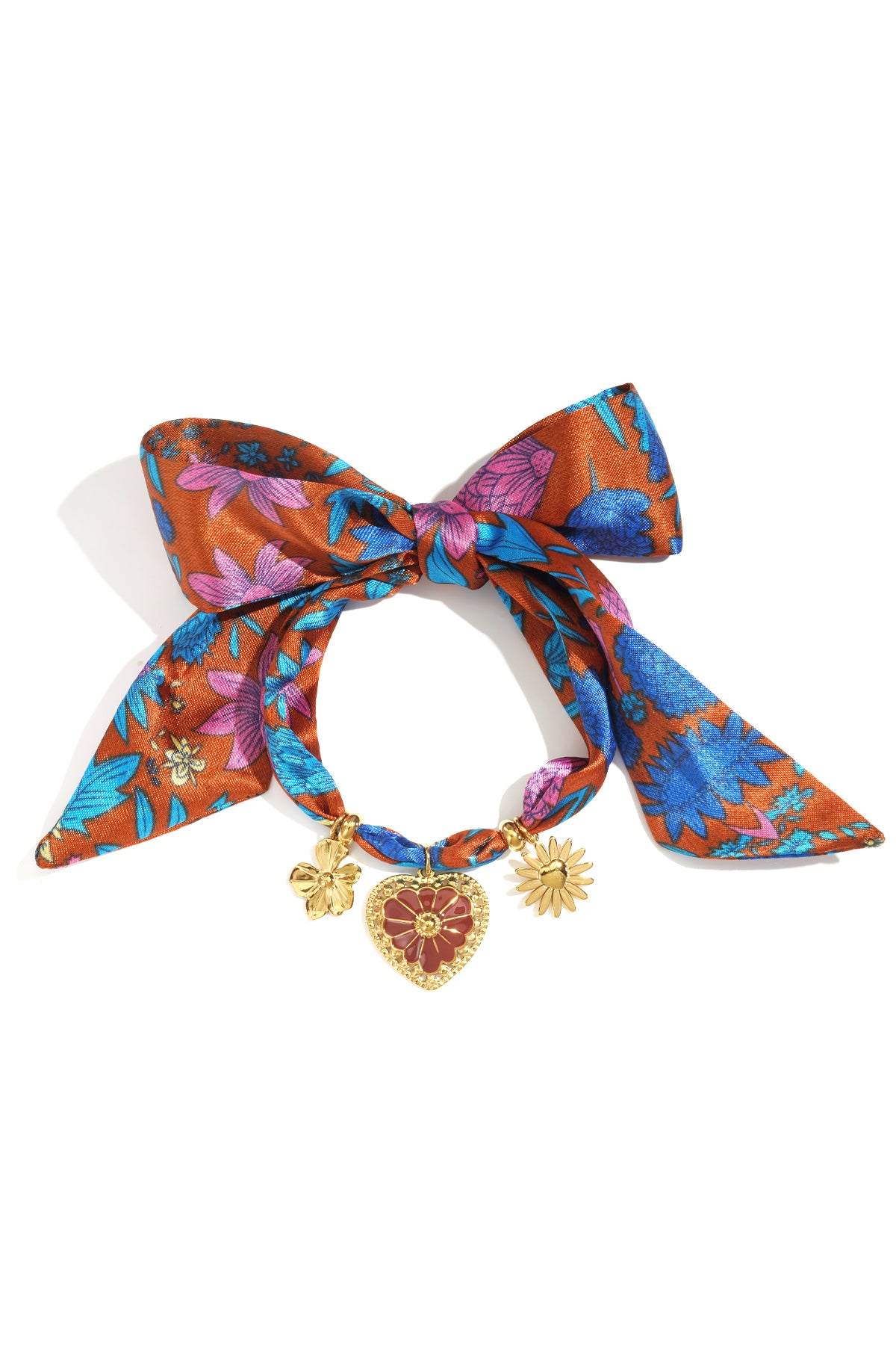 Close-up of a floral charm bracelet featuring a burnt orange fabric with blue and pink flowers tied in a bow, adorned with gold-tone flower and heart charms