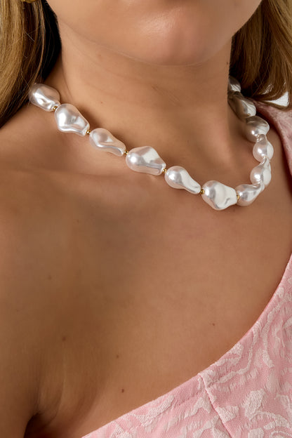 Close-up of a woman wearing the baroque imitation pearl necklace, paired with a pink textured off-shoulder top