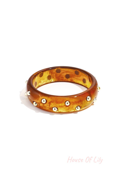 Dark amber marbled resin bangle with shiny gold studs isolated on white background