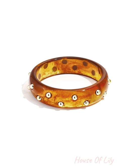 Dark amber marbled resin bangle with shiny gold studs isolated on white background