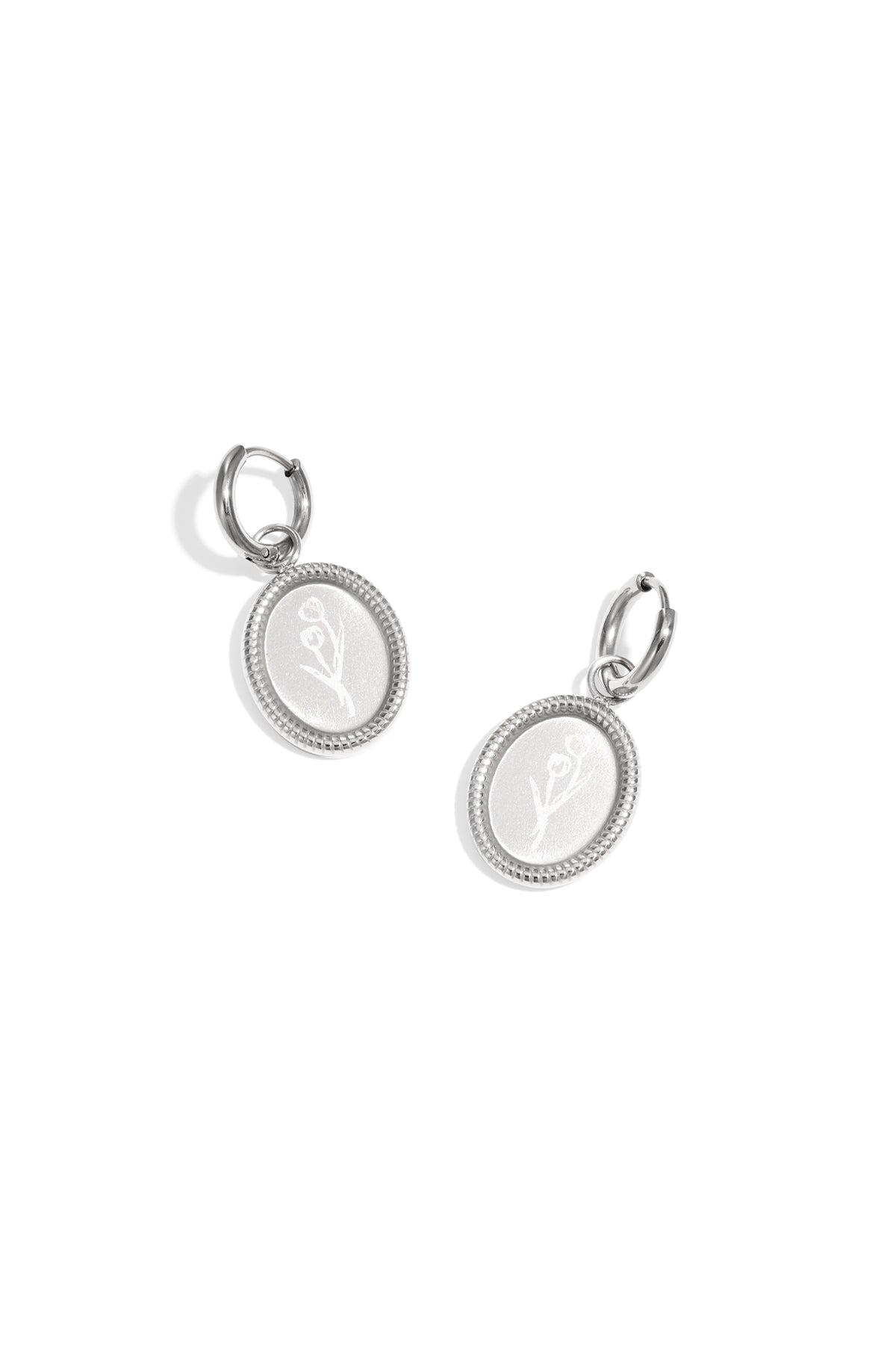 Pair of silver oval hoop earrings with embossed floral design on white background
