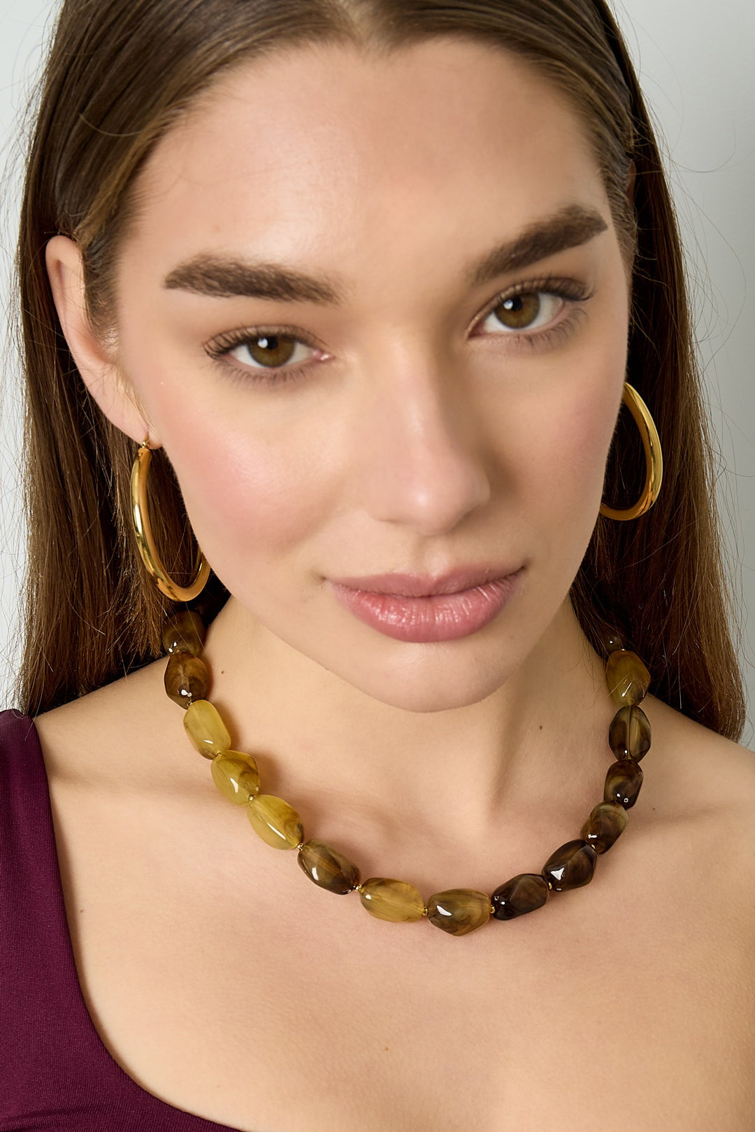 Close-up of woman wearing amber and chocolate-colored chunky beaded necklace with gold hoop earrings