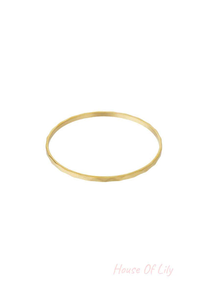 Single thin minimalist hammered gold-tone bangle on white background