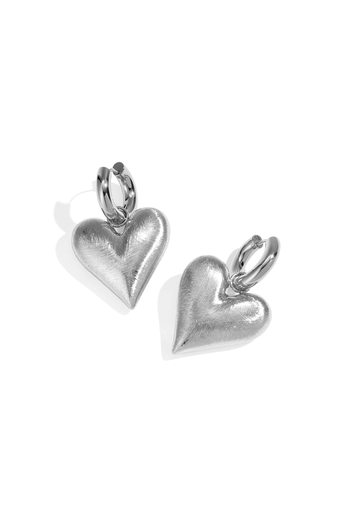 Pair of silver heart charm drop earrings with brushed texture on white background