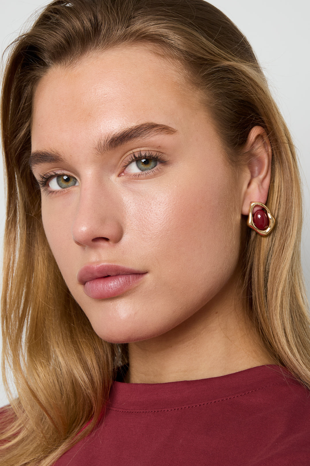 Golden Glitch Hoops: gold-toned, irregularly shaped huggie earrings featuring a central, polished dark-red cabochon stone.