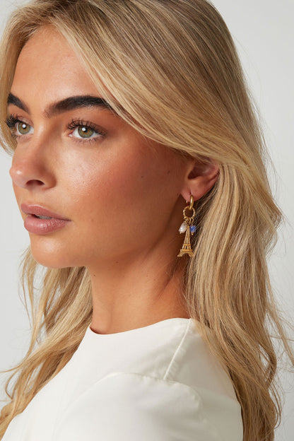 Close-up side view of blonde woman wearing gold-tone Paris Eiffel Tower charm earrings with pearls and purple beads