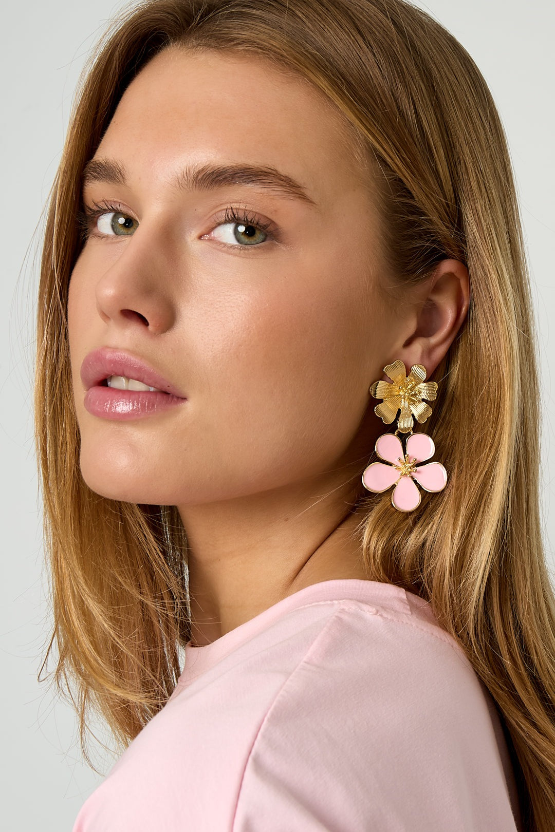 Model wearing pink enamel floral drop earrings with gold textured flowers, showcasing youthful boutique style
