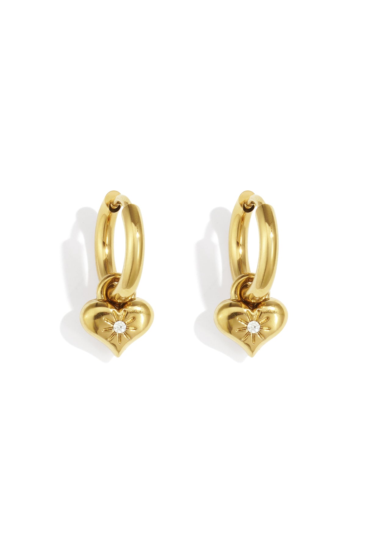 Pair of golden hoop earrings with heart-shaped charms featuring a central rhinestone in a sunburst design on white background