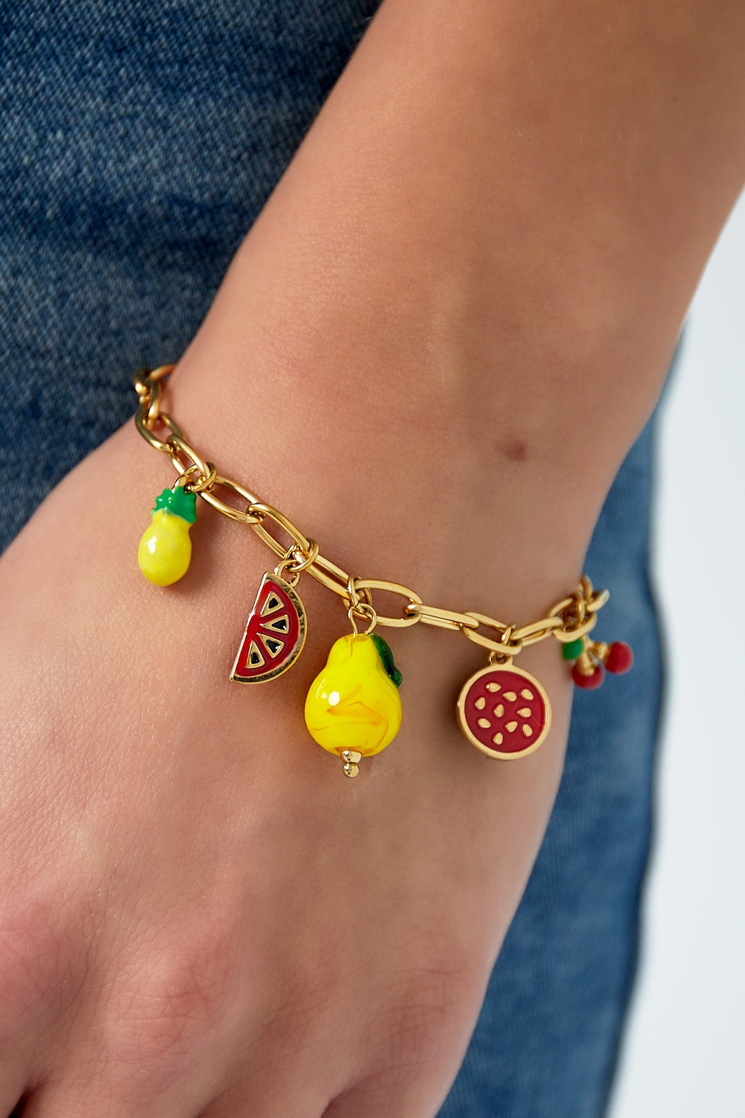 Close-up photo of the gold chain fruit charm bracelet worn on a wrist with denim background