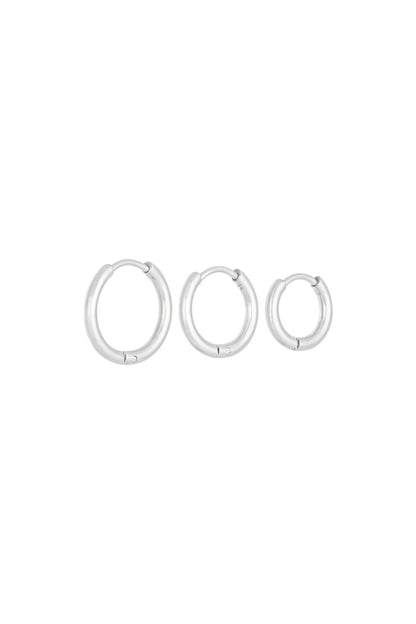 Three silver stainless steel hoop earrings of different sizes lined up on a white background