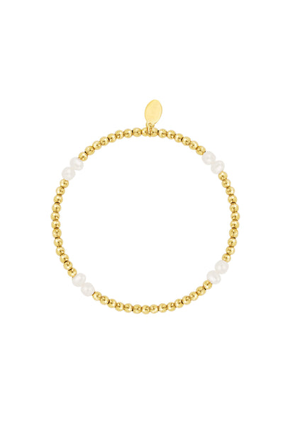 Styled view of gold bead and white pearl bracelet with branded charm on white background