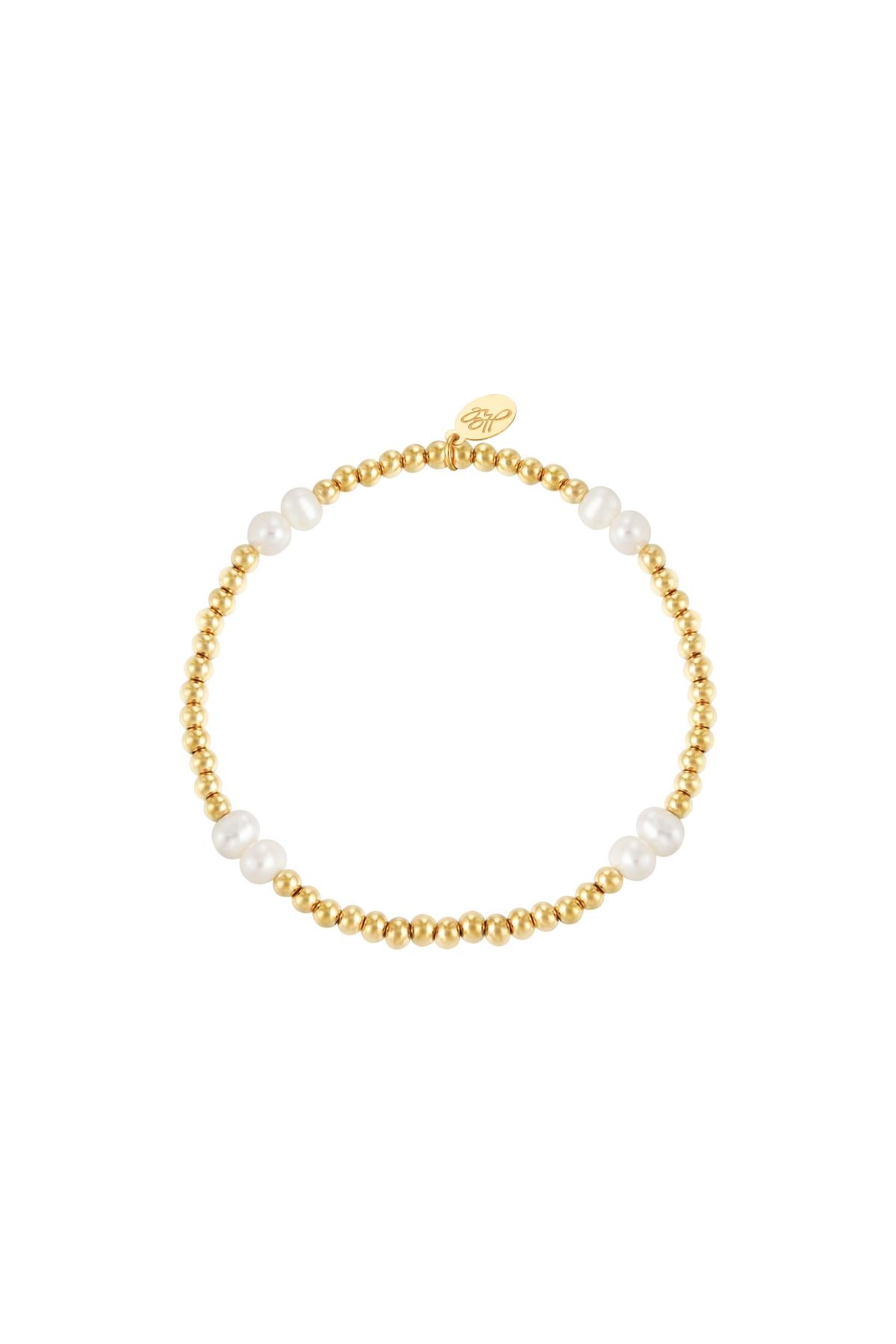 Gold color beaded bracelet with white pearls and a small gold charm on white background