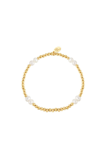 Gold color beaded bracelet with white pearls and a small gold charm on white background