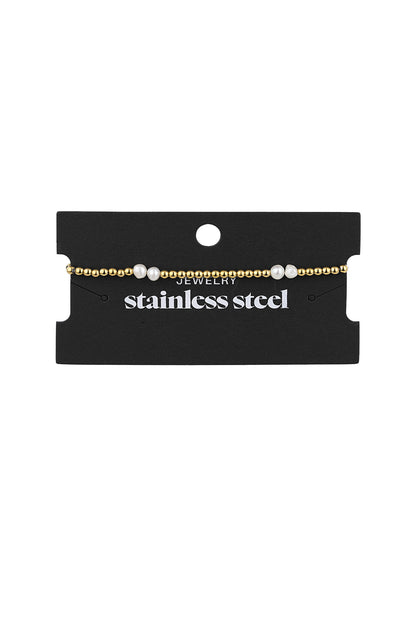 Gold and pearl beaded bracelet displayed on black jewelry card showing stainless steel label