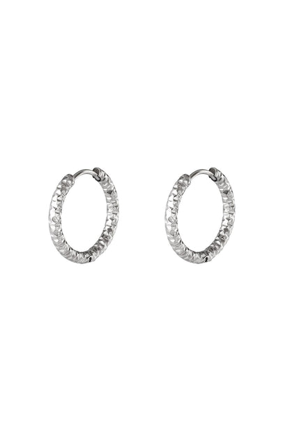 Pair of silver textured hoop earrings with hammered pattern on white background