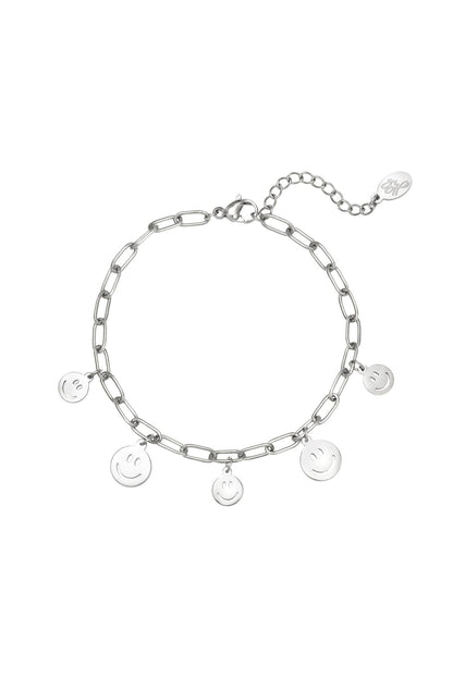 Silver tone link chain bracelet with five dangling smiley face charms and lobster clasp on white background