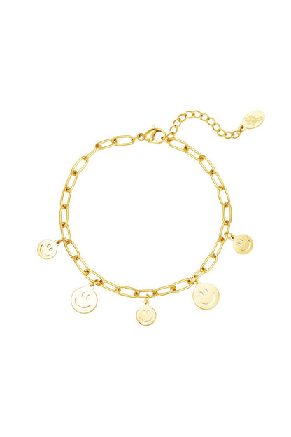 Gold tone link chain bracelet with five dangling smiley face charms and lobster clasp on white background
