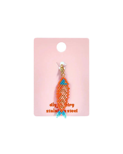 Orange and blue seed bead fish charm with a gold clasp on a pink backing card.