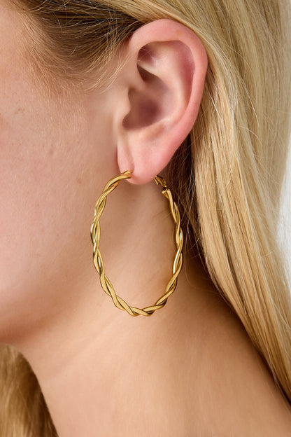 Close-up of gold twisted oval hoop earring worn on a woman’s ear with blond hair
