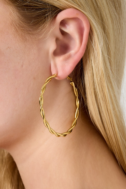 Close-up of gold twisted oval hoop earring worn on a woman’s ear with blond hair