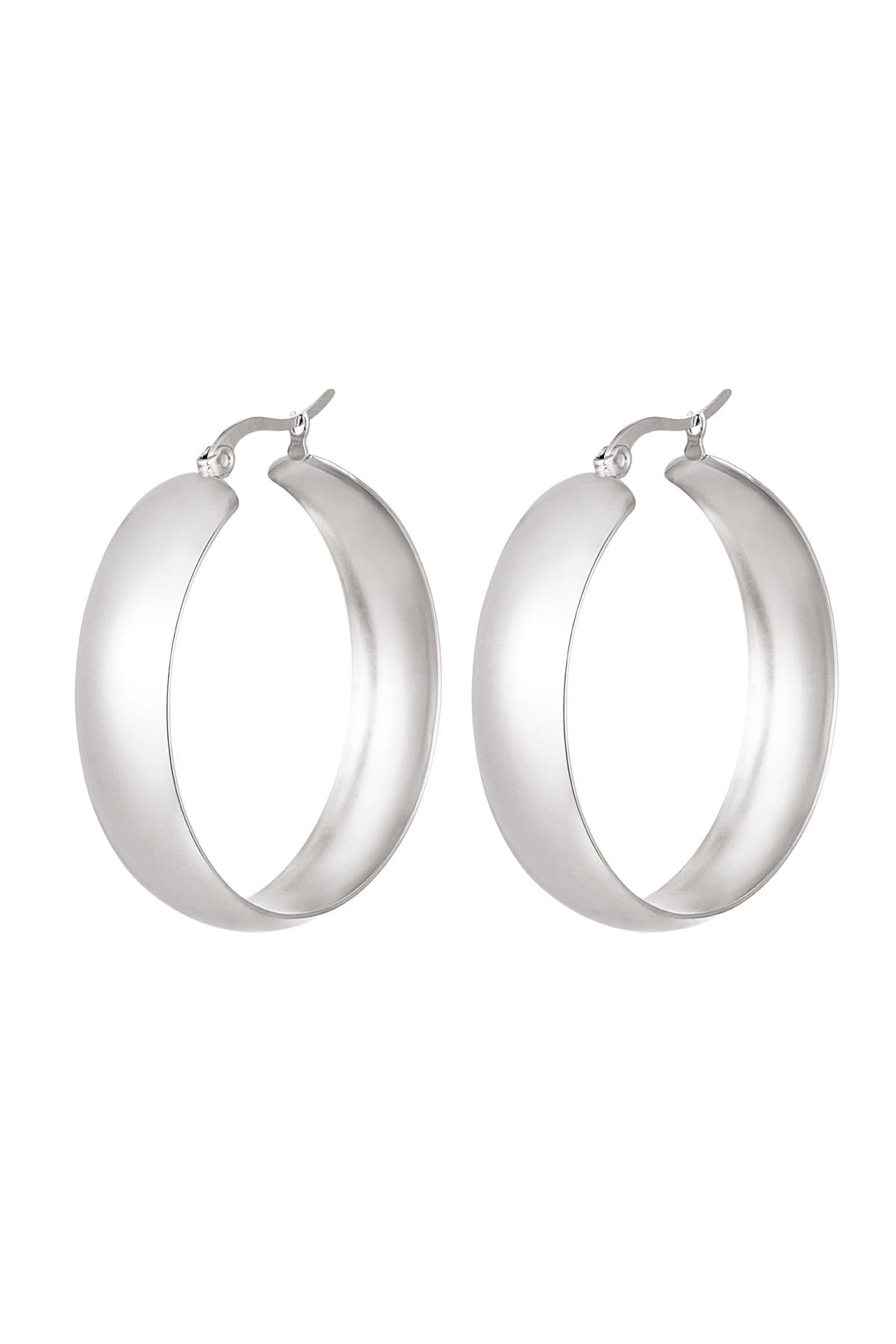 Pair of bold, wide silver hoop earrings with a smooth curved design on a white background