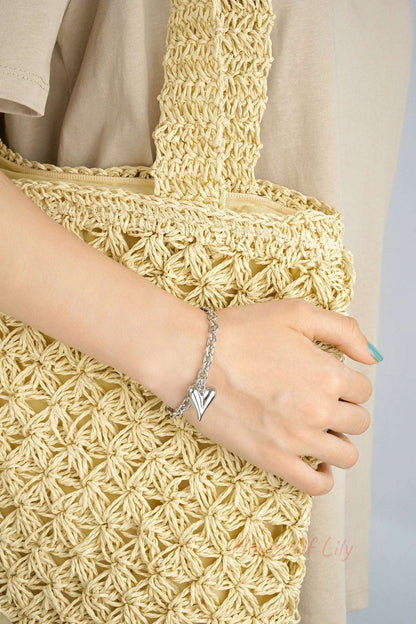 Silver chunky heart charm bracelet worn on wrist holding a woven beige tote bag