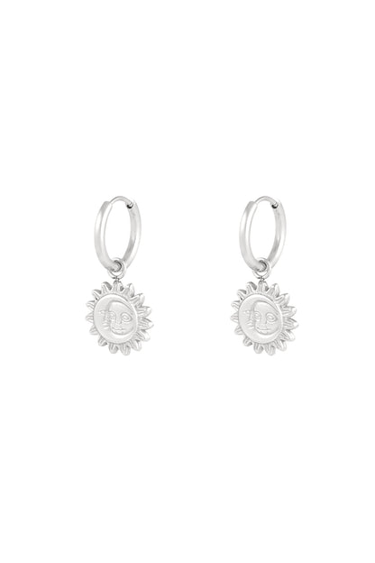 Close-up of silver hoop earrings with sun-shaped dangling charms featuring a smiling face design on white background
