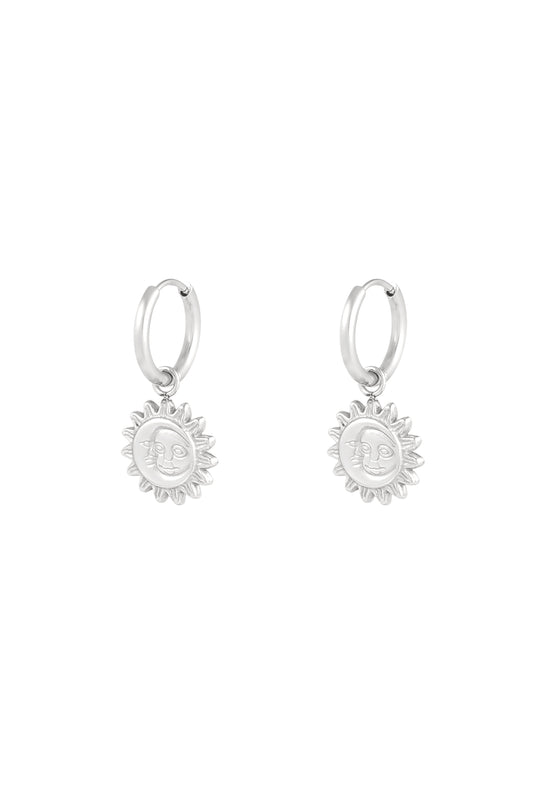 Close-up of silver hoop earrings with sun-shaped dangling charms featuring a smiling face design on white background