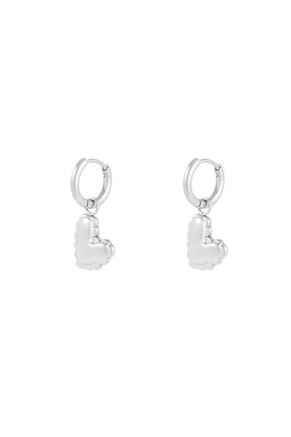Close-up of silver heart charm drop earrings with scalloped puffed heart design against white background