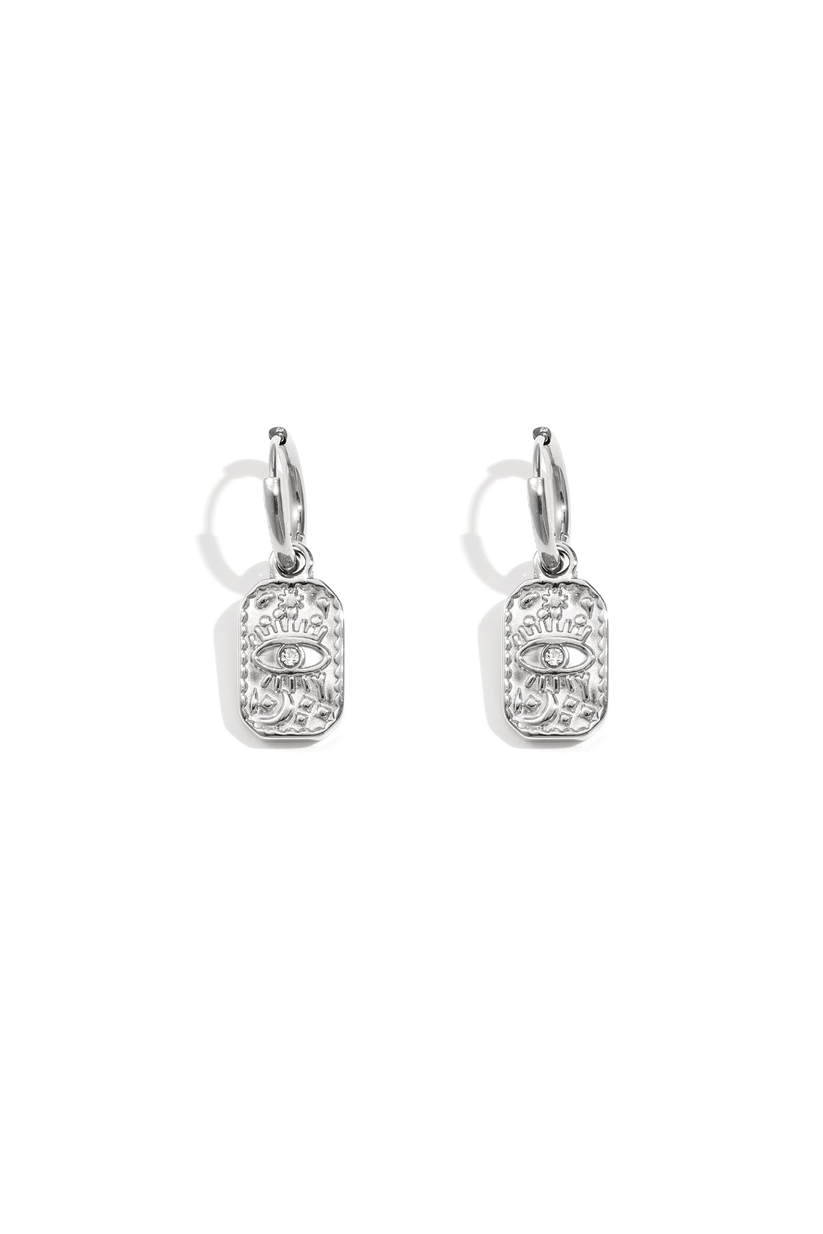 Pair of silver hoop earrings with a rectangular charm embossed with an eye motif and small rhinestone on white background