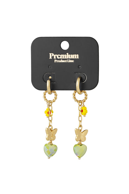 Pair of gold drop earrings with yellow flower and green heart charm displayed on black Premium Product Line card