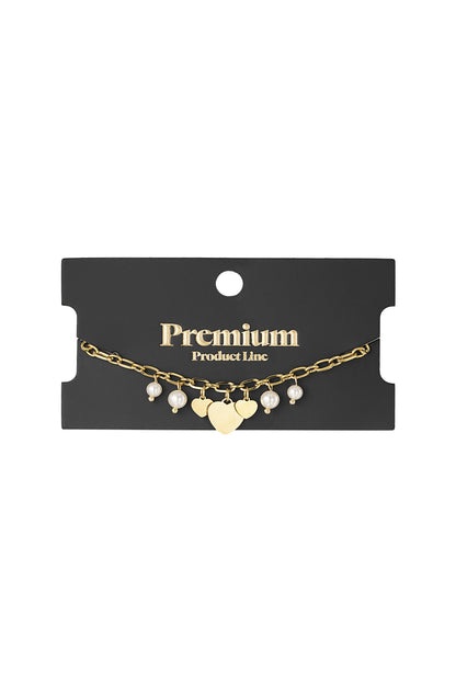 Gold finish charm bracelet displayed on black Premium Product Line card, showcasing heart charms and pearl accents.