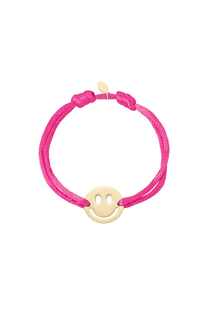 Close-up of pink satin cord bracelet with gold-tone smiley charm