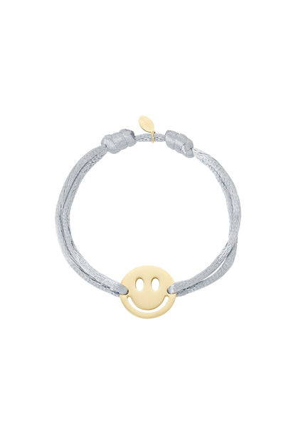 Red satin cord bracelet with gold-tone smiley face charm on white background