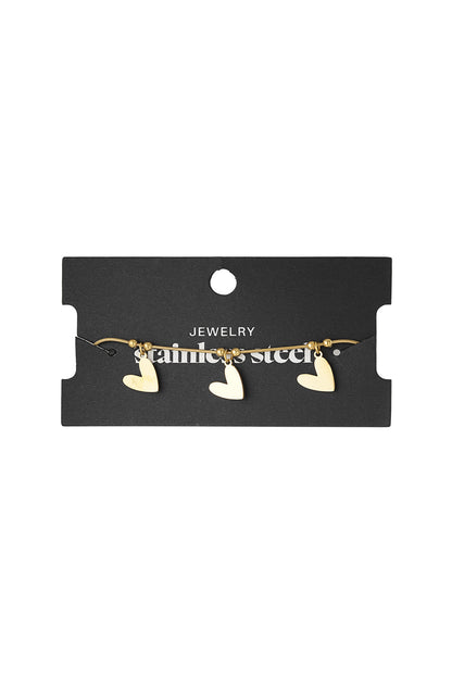 Gold heart charm bracelet displayed on black jewelry card with stainless steel label