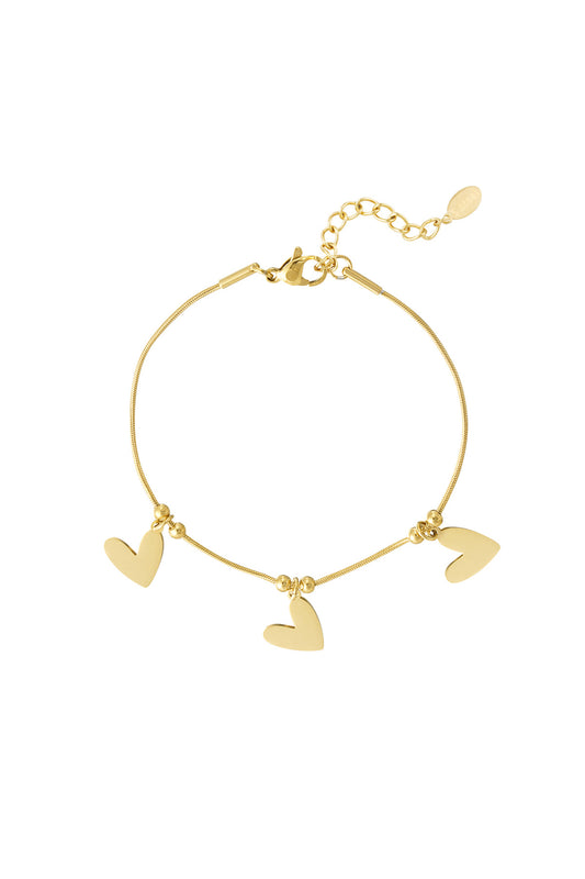 Gold heart charm bracelet with three flat heart pendants and adjustable chain on white background
