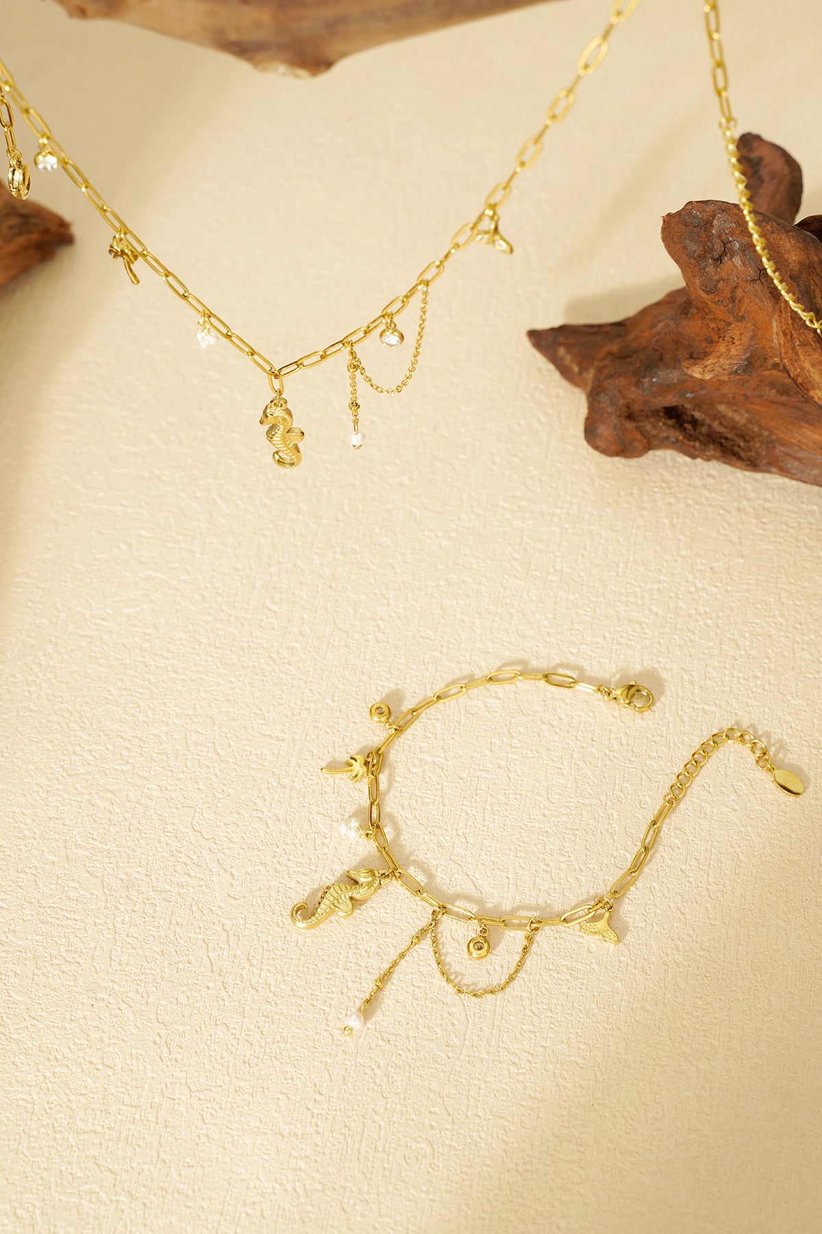 Gold charm bracelet displayed flat on textured cream background featuring ocean-inspired charms