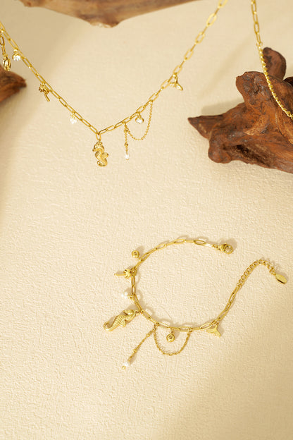 Gold charm bracelet displayed flat on textured cream background featuring ocean-inspired charms