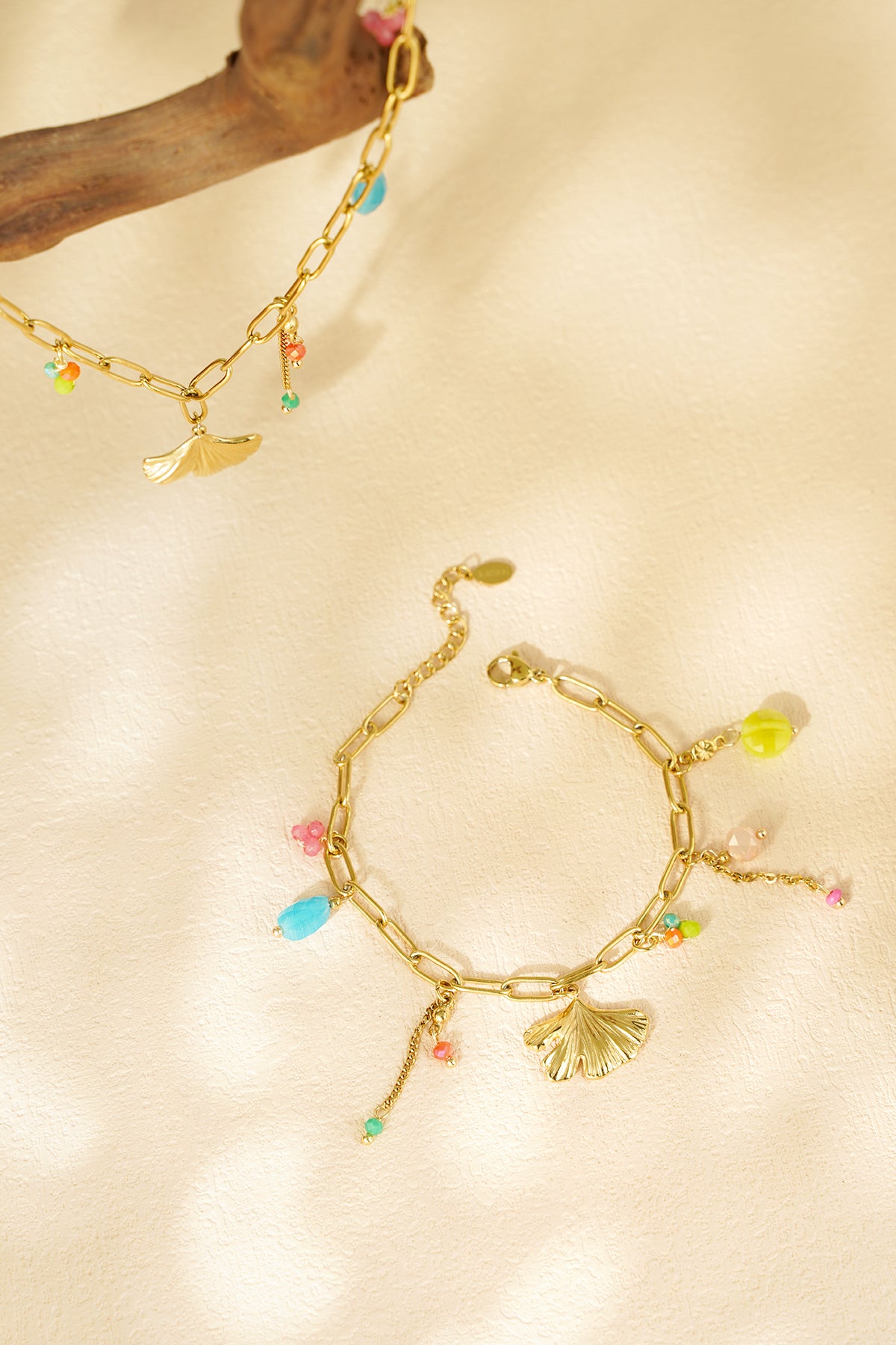 Lifestyle shot of the gold charm bracelet with blue, pink, orange and green beads on textured cream background