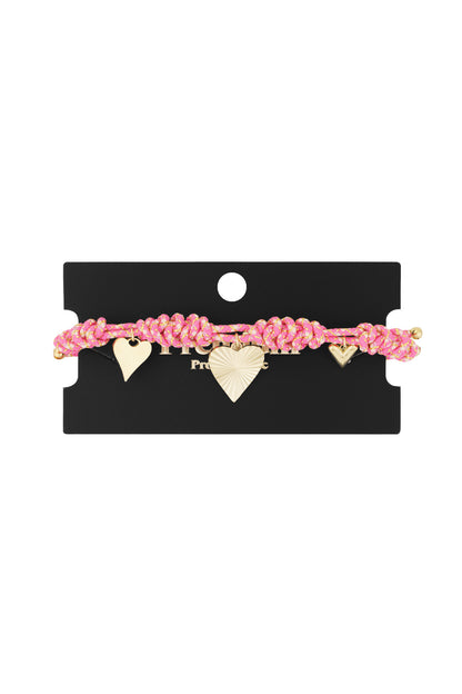 Pink braided bracelet with gold-tone heart charms displayed on black jewelry card
