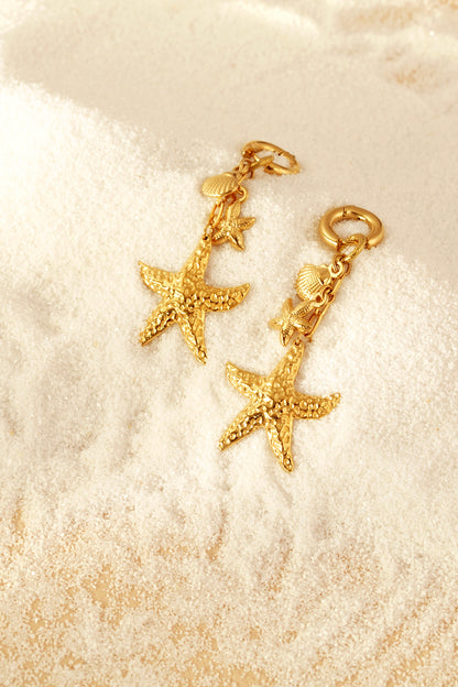 Gold starfish and seashell drop earrings resting on fine white sand