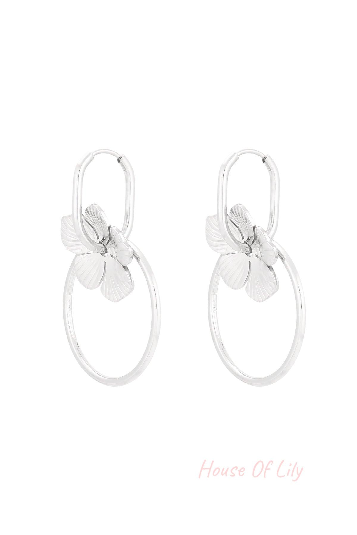 Pair of silver-tone floral hoop drop earrings with flower charms and circular hoops on white background